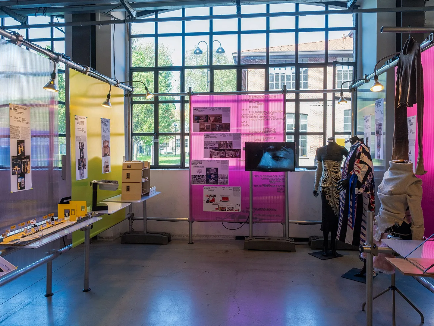 An exhibition area with garments on mannequins and magenta panels in front of a large window